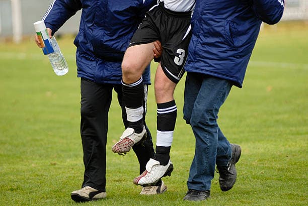 Two coaches helping an injured soccer player off the field after a sports injury